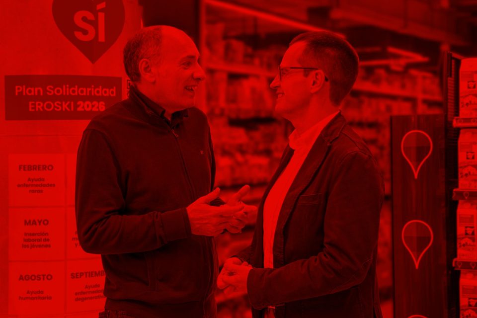 Dos hombres conversando en un supermercado junto a un panel del Plan Solidaridad 2026.