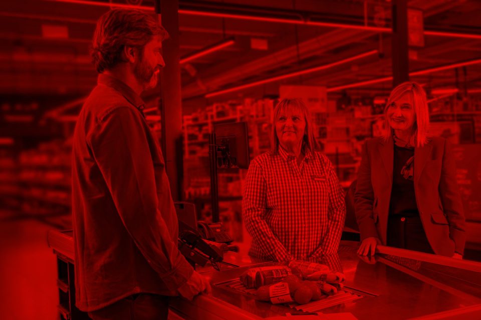 Cliente conversando con dos trabajadoras de EROSKI en la zona de cajas del supermercado.