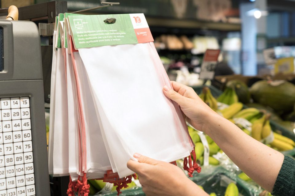 Persona seleccionant bosses reutilitzables per a fruita i verdura en la secció de frescos d'un supermercat.