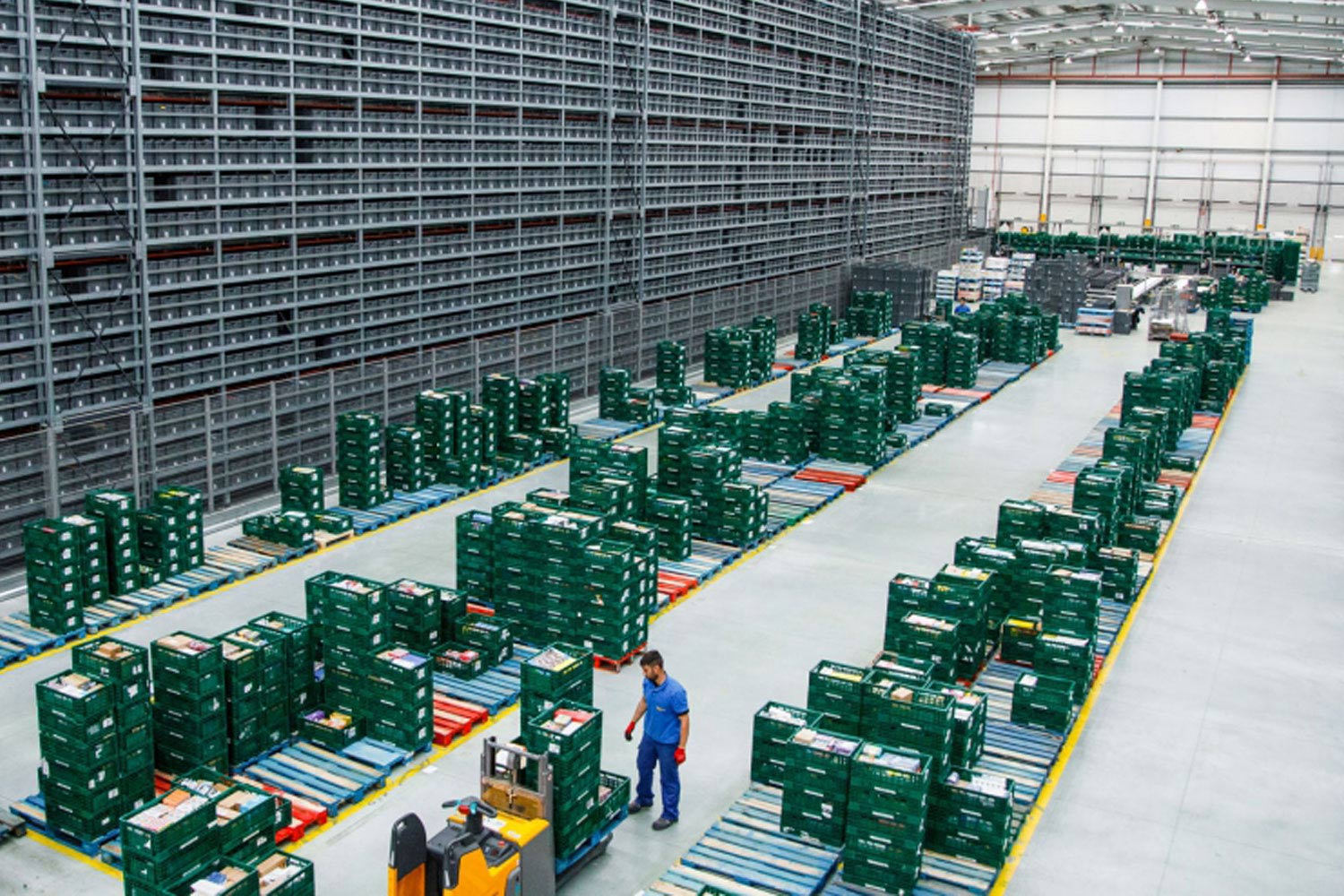 Centre logístic automatitzat amb caixes de distribució sobre cintes transportadores i operari supervisant la zona.
