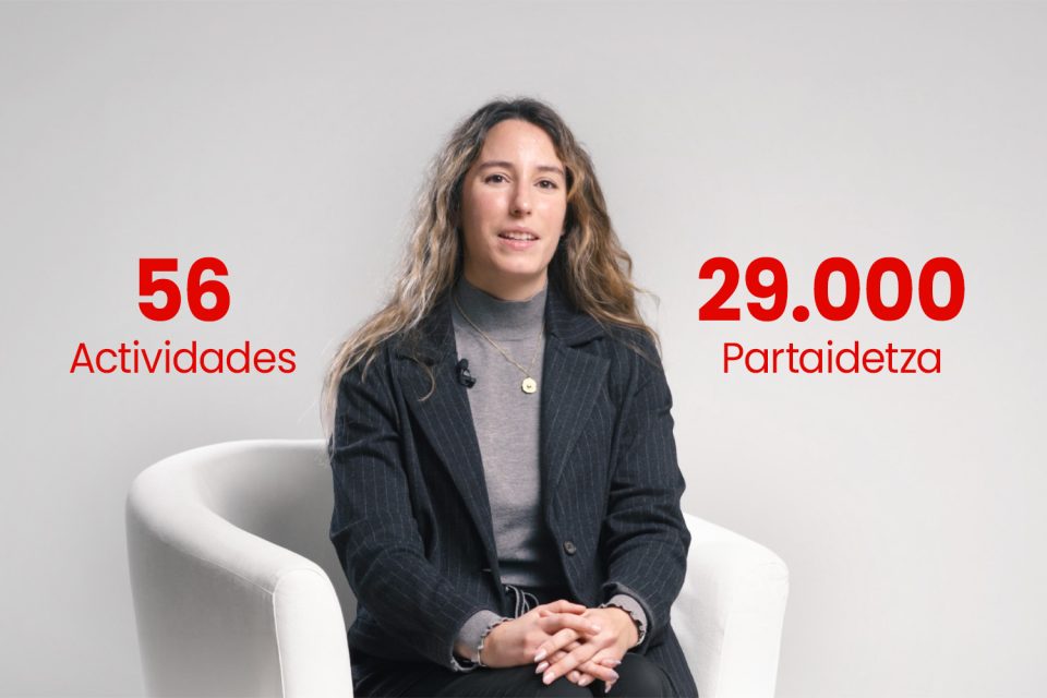 Dona asseguda en una butaca en una entrevista corporativa amb dades destacades sobre activitats i participació en pantalla.
