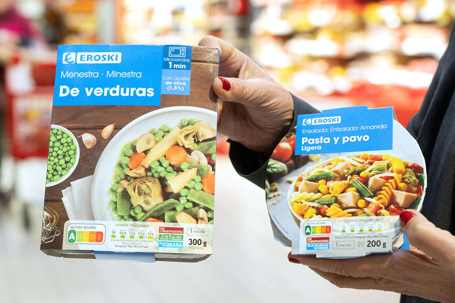 Persona sostenint dos productes preparats EROSKI de verdures i pasta amb informació nutricional visible.