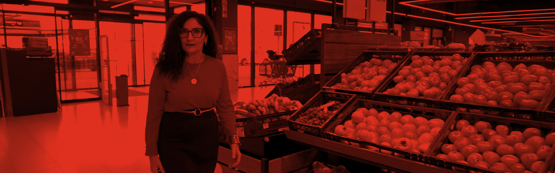 Mujer caminando junto a la sección de frutas y verduras en un supermercado EROSKI.